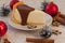 A a piece of an appetizing cheese cake with melted chocolate on it, silver cones, cinnamon sticks and Christmas-t