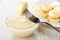 Piece of banana strung on fork in bowl with condensed milk, plate with slices of banana on table