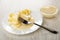 Piece of banana strung on fork in plate with slices of banana and condensed milk, bowl with milk on table