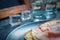 A piece of bread with slice of pork and shots of vodka on wooden background