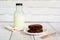 Piece of brownie cake on white small plate with bottle of fresh milk on wooden table and with brick wall with copy space