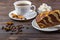 A piece of cake with a cup of coffee. Cinnamon sticks, anise, fork and a bowl with sugar cubes on dark wooden background