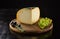 Piece of cheese, black olives and grapes on wooden board