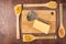A piece of cheese and a metal grater on a bamboo cutting Board surrounded by spatulas with various pastes on a wooden background