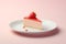 Piece of a cheesecake topped wit one fresh strawberry on a white plate, side view over minimalist pink background with copy space
