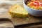 A piece of cornbread on a vintage cutting board shown with a bowl of chili.