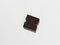 A piece of dark chocolate bar on a white paper background. A hard shadow. Sweet and high-calorie product. Top view, flat lay