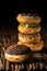 A piece of donut on wooden plank with a stack of donuts behind on dark background