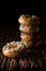 A piece of donut on wooden plank with a stack of donuts behind on dark background