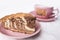 A piece of freshly baked pie Zebra in a saucer mauve pink colour and a cup of tea in a defocus