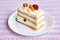 Piece of fruit yogurt cake with fresh strawberry, raspberry, peach, grapes and almonds on a white plate and pattern background.