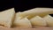 A piece of hard cheese falls into a pile of sliced sheep`s cheese close-up.