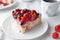 A piece of home-made cottage cheese berry pie. Garnished with cream, strawberries, blueberries, sea buckthorn berries. On a white