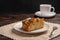 Piece of homemade traditional cornish apple pie on a white plate with a fork on a napkin. Cup of tea in the background