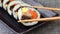 Piece of korean dish gimbap or kimbap with tuna and vegetables taken from plate with chopsticks