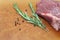 A piece of large piece of marbled beef lying on a wooden board with sprigs of rosemary, salt and pepper