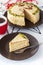 Piece of Mocha coffee layered cake with butter cream, pistachio, mug in red knit shirt, close-up white background.