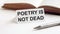 Piece of paper with text Poetry Is Not Dead on the background of books, pens, on a white background
