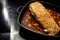 Piece of pork meat with incised fat rind on a brown sauce base from vegetables and red wine in a black cooking pan on the stove