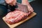 Piece of pork neck cutout on woodwn table. Man cutting meat