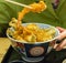 Piece of prawn tempura held by chopsticks above bowl of various fish and vegetable tempura, Kanazawa, Ishikawa Prefecture,Japan