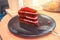 A piece of red velvet cake on a brown round plate with forks and