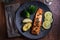 A piece of roasted salmon grilled lemon pepper and salt on a dark plate with broccoli. Wood background