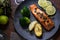 A piece of roasted salmon grilled lemon pepper and salt on a dark plate with broccoli. Wood background