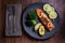 A piece of roasted salmon grilled lemon pepper and salt on a dark plate with broccoli. Wood background