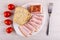 Piece, slices of brisket, bread in dish, fork, tomato cherry on table. Top view