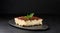 A piece of tiramisu sprinkled with cocoa, on top of a sprig of fresh mint on a black background