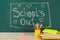 Pieces of chalk and stationery on table near greenboard with text School`s Out. Summer holidays