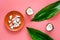 Pieces of coconut flesh on plate on pink background with coconut cut in half and palm leaves top view