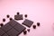Pieces of dark chocolate bar and milk chocolate pearls on pink background, top view, copy space