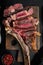 Pieces of delicious barbecued meat medium rare beef steak,  tomahawk cut, on wooden serving board, on black stone background, top