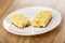 Pieces of granola bar with corn flakes, puffed rice, coconut and chocolate in saucer on wooden table