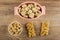 Pieces of halva in oval bowl, peanuts in white bowl, pieces of kozinak on table. Top view