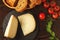 Pieces of hard cheese on slate dish, parsley, thyme, grain bread and cherry tomatoes on a wooden table, top view, flat