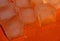 Pieces of ice on a bright background with water drops. Orange fresh background with ice cubes