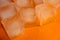 Pieces of ice on a bright background with water drops. Orange fresh background with ice cubes