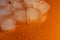 Pieces of ice on a bright background with water drops. Orange fresh background with ice flakes