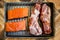 Pieces of pork and pieces of salmon on rack in broiling pan ready to cook sitting on rustic wood surface