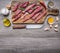 pieces raw beef on a cutting board with a knife, butter and seasonings, border, with text area on wooden rustic background top v