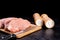 Pieces of raw meat on wooden board next to salt and pepper shake