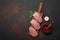 Pieces of raw pork steak with basil, garlic, pepper, salt and spice mortar on cutting board and rusty brown background with space