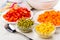 Pieces of sweet pepper, carrot in plates, green peas and corn in bowls, spoon, napkin on table