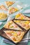 Pieces of tarte flambee with salmon, yellow pepper and spring onions on a wooden board on light green background
