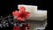 Pieces of white natural soap with water drops and red flower on a black glossy surface, close-up, selective focus