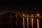 A pier at night: lamp lights, a blurry group of fishermen and a distant silhouette of Mount Victoria