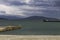 Pier on the sea beach and the lighthouse on the background of mountains and overcast sky.